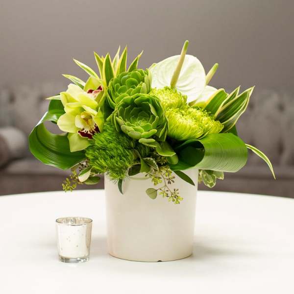 Green floral arrangement in a white vase with orchids and anthurium