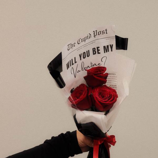 Handheld bouquet of red roses wrapped in black and white paper