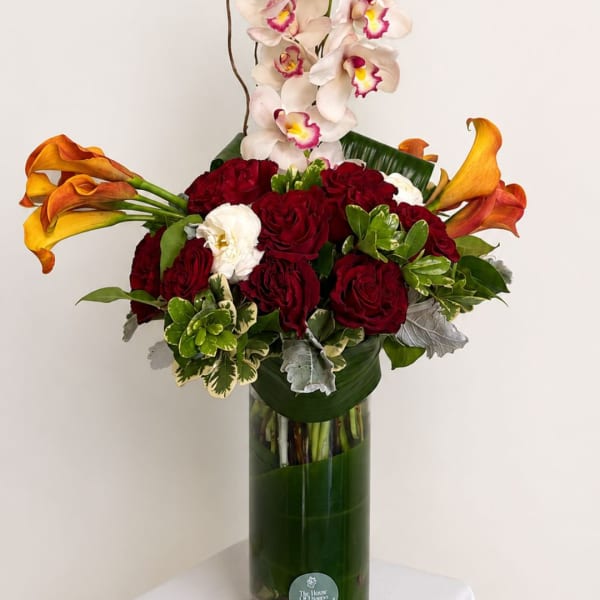 Red roses and calla lilies with white orchids in a tall glass vase