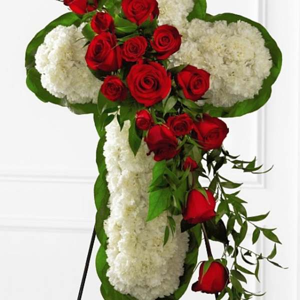 Cross-shaped floral tribute with red roses and white carnations on a stand