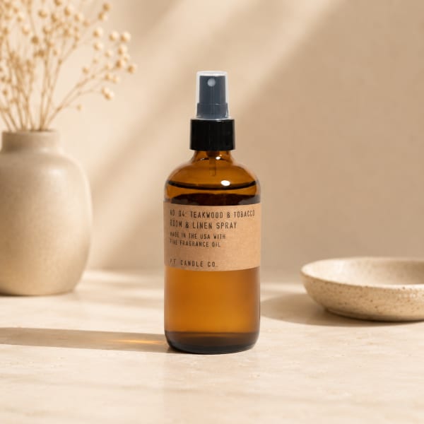 Amber room spray bottle on a neutral tabletop with a vase and bowl nearby