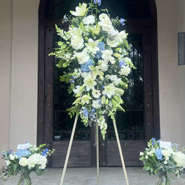 Large standing floral spray with white and blue flowers on a tripod easel