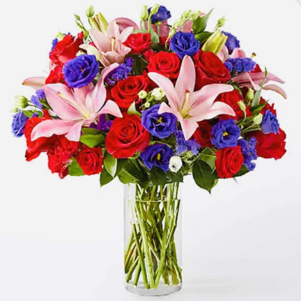 Bouquet of red roses, pink lilies, and purple blooms in a clear glass vase