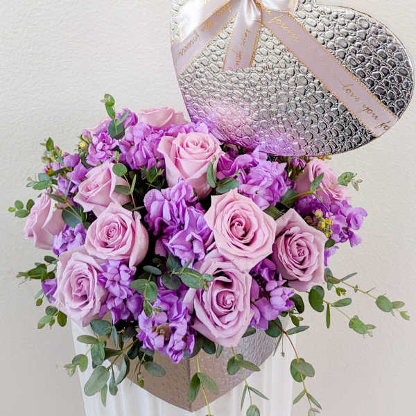 Pink roses and purple flowers in a silver heart-shaped box with a ribbon