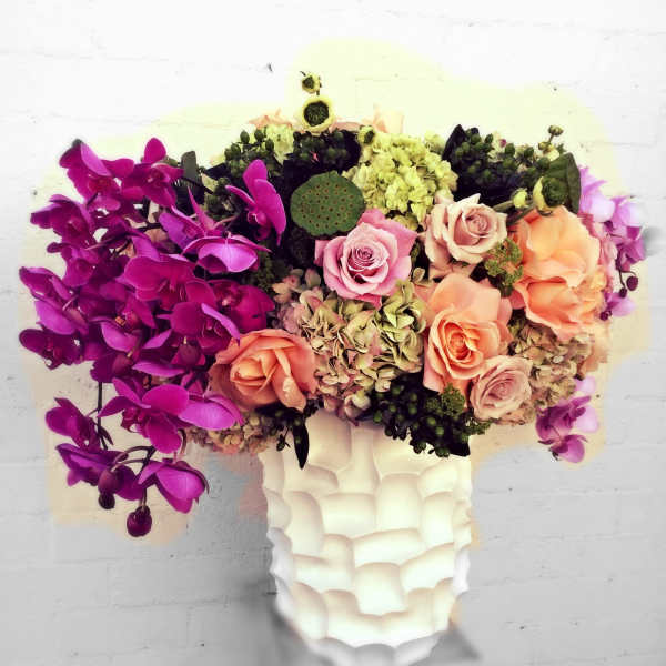 Mixed bouquet of orchids, roses, and hydrangeas in a white vase