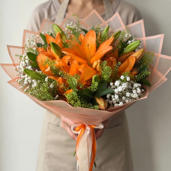 Orange lily bouquet wrapped in peach paper with white filler flowers