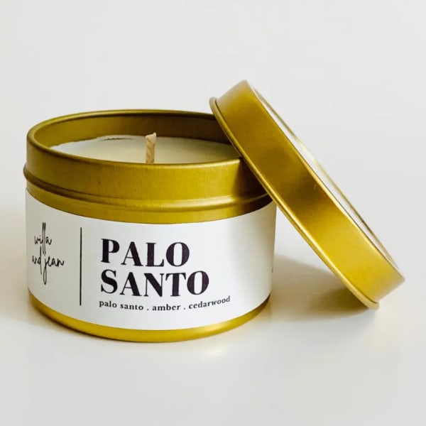 Gold tin candle labeled Palo Santo with lid leaning beside it