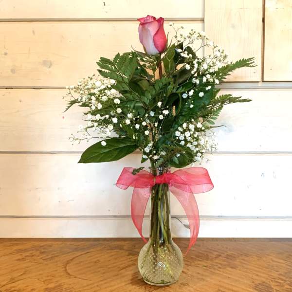 Single pink rose in a glass vase with baby's breath and a pink ribbon