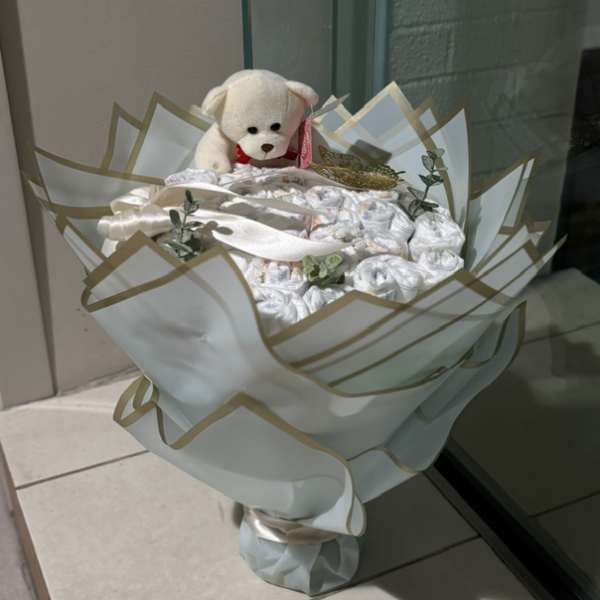 White teddy bear atop a wrapped bouquet of white rolled items