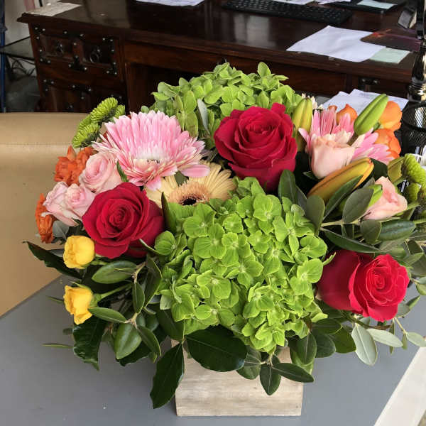 Mixed bouquet with red roses, pink blooms, and green hydrangeas in a square vase