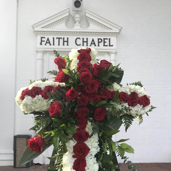 Large cross-shaped floral tribute with red roses and white flowers on an easel