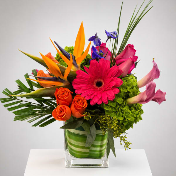 Bright mixed bouquet in a square glass vase with orange, pink, and purple blooms