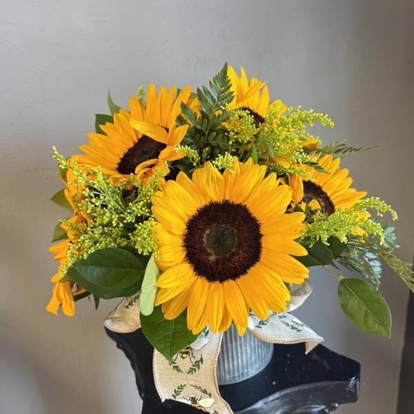 Bouquet of yellow sunflowers in a ribbed metal container with a ribbon