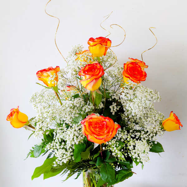 Orange-yellow roses in a clear glass vase with white baby's breath
