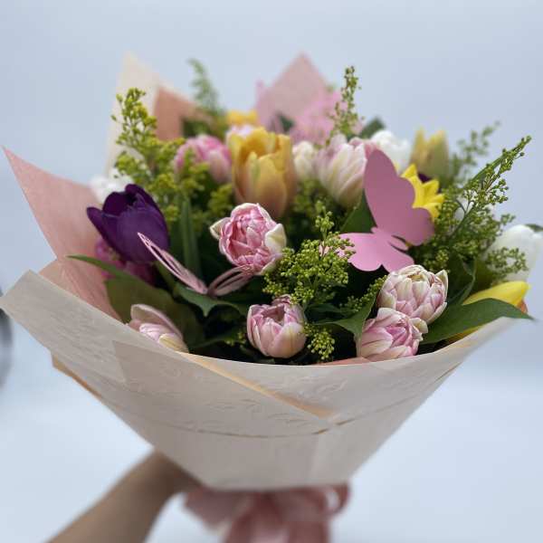 Handheld bouquet of pink, yellow, and purple tulips wrapped in pale paper