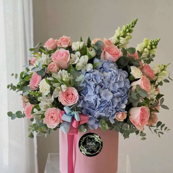 Pink roses and blue hydrangea in a pink hatbox with ribbon