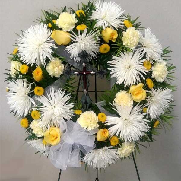 White and yellow floral wreath on a stand with a white bow