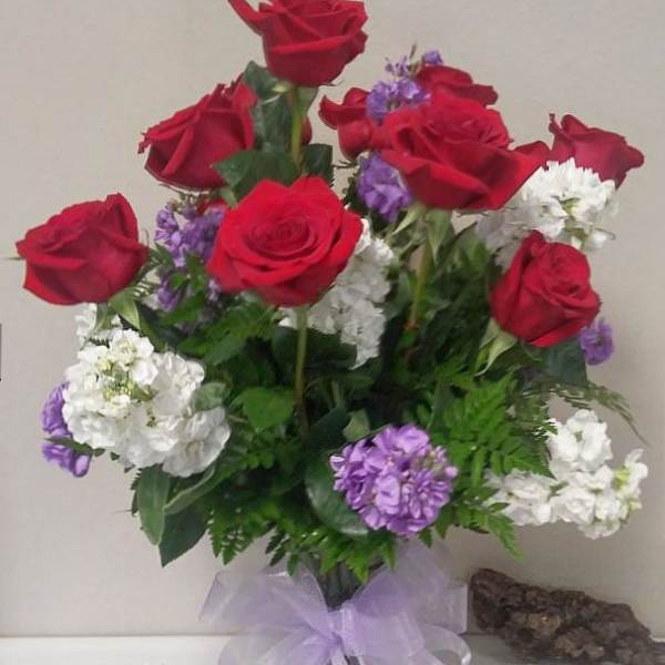 Red roses with white and purple flowers in a glass vase with a lavender bow