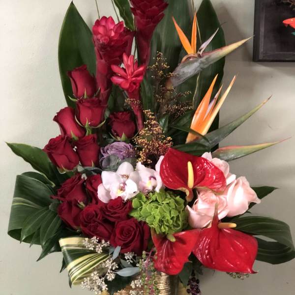 Tall tropical bouquet with red roses, anthuriums, and orchids in a gold vase