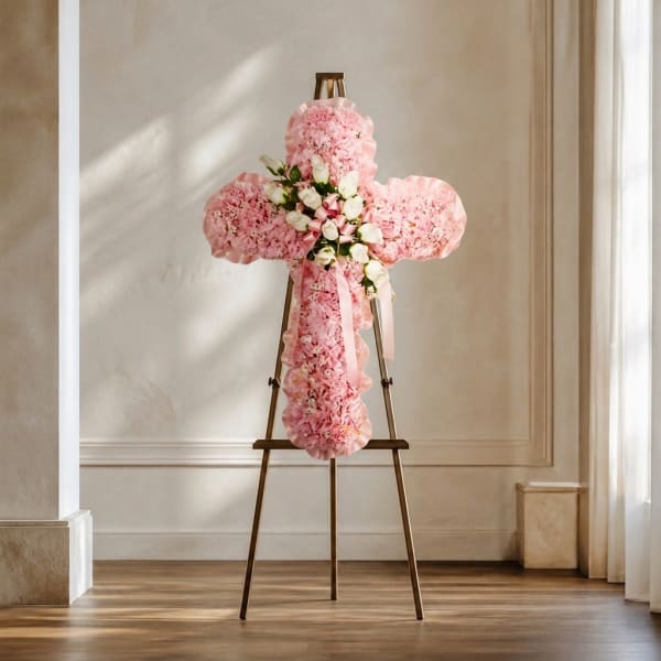 Pink floral cross arrangement on a stand with a ribbon bow