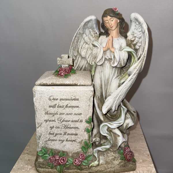 Angel figurine beside a memorial box decorated with pink roses