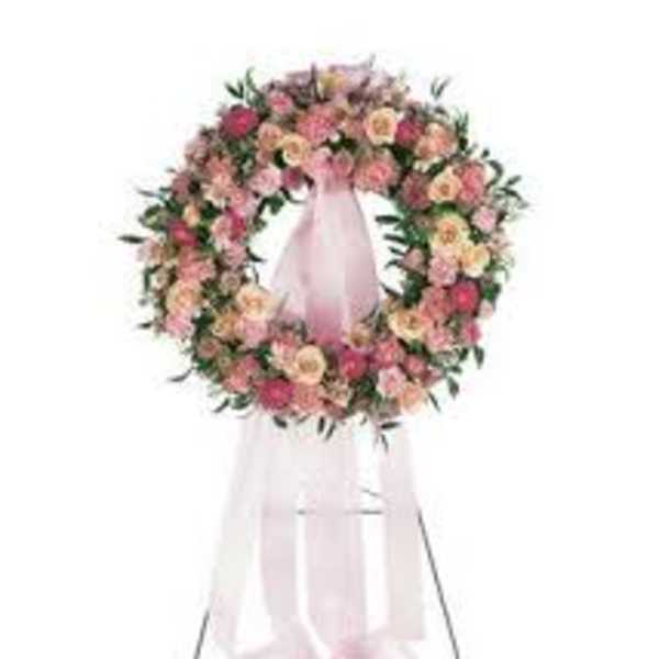 Pink and peach floral wreath on a white stand with a sheer ribbon