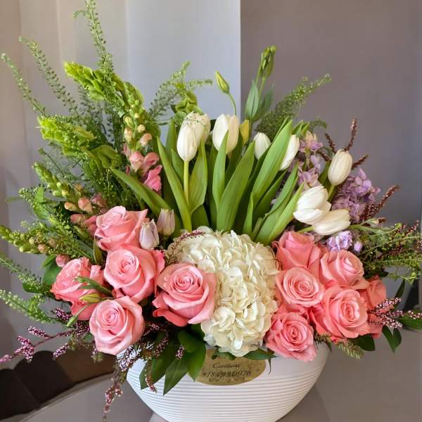 Pink roses and white tulips arranged in a white bowl vase