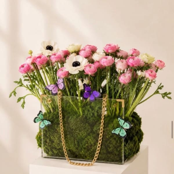 Pink and white flowers arranged in a clear box with a gold chain handle