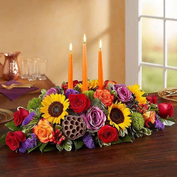 Low floral centerpiece with lit orange candles and mixed roses and sunflowers