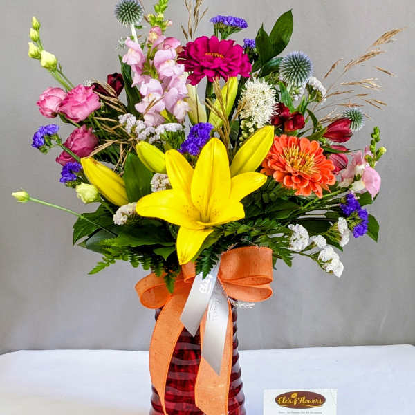Colorful mixed bouquet in a red glass vase with an orange ribbon