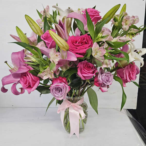 Pink roses and lilies arranged in a glass vase with a pink ribbon.