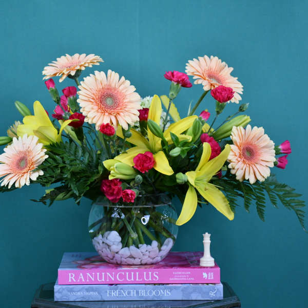 Mixed bouquet of gerbera daisies, lilies, and carnations in a glass bowl vase