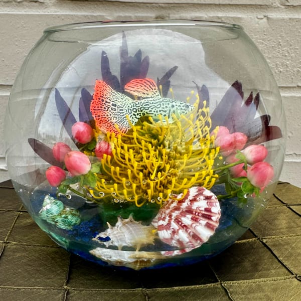 Fishbowl arrangement with a yellow flower, pink buds, and seashells