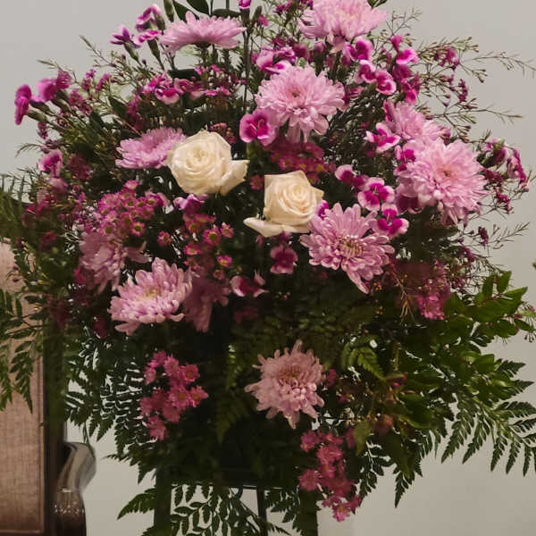 Pink and white floral arrangement with roses and daisies on a stand