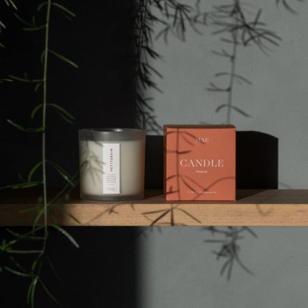 A scented candle in a frosted glass jar beside its coral box