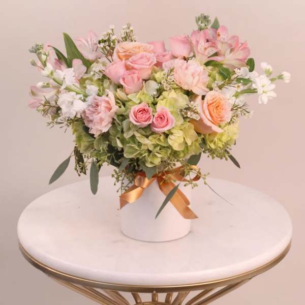 Pink and peach roses arranged with white blooms in a white vase