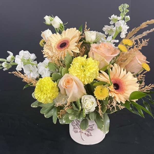 Mixed bouquet of peach roses, gerbera daisies, and yellow carnations in a white vase