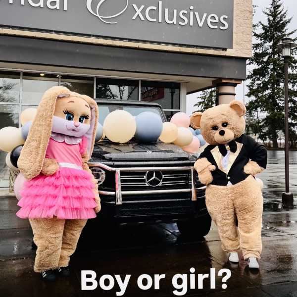 Bunny and bear mascots pose by a balloon-decorated black SUV in front of a bridal shop.