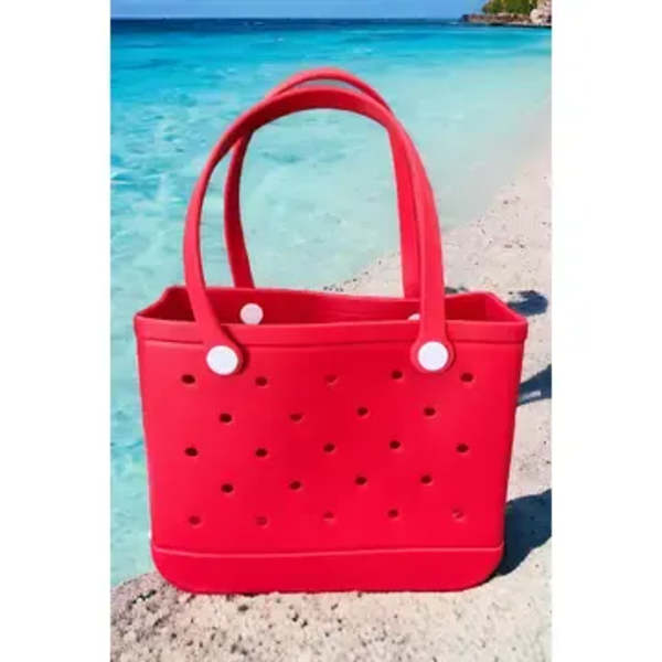 Red perforated tote bag on a beach with turquoise water