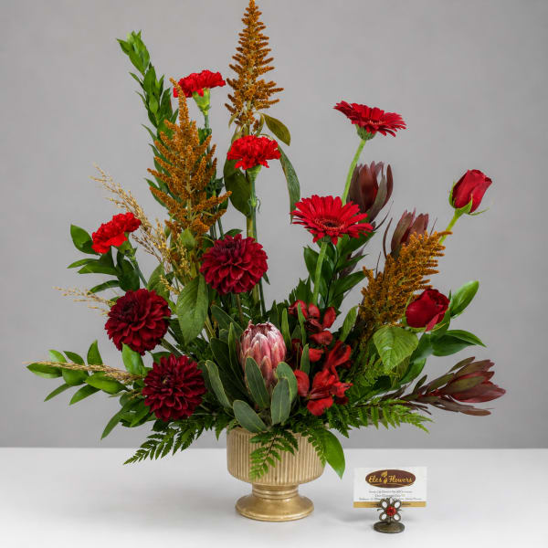 Red floral arrangement in a gold vase with tall mixed blooms