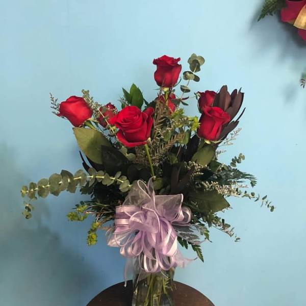 Red roses in a glass vase with a lavender ribbon bow