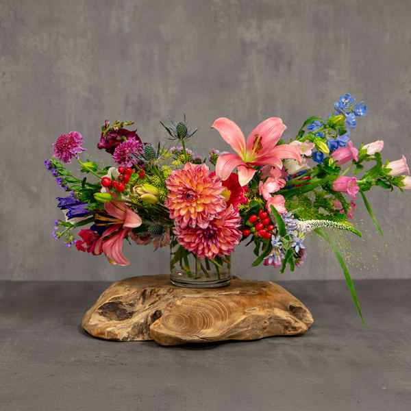 Colorful mixed bouquet in a clear glass vase on a wooden base