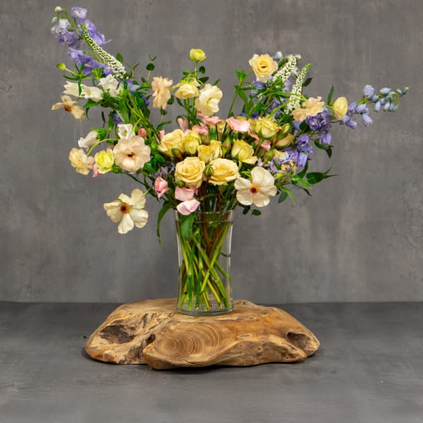 Mixed pastel flowers in a clear glass vase on a wooden base