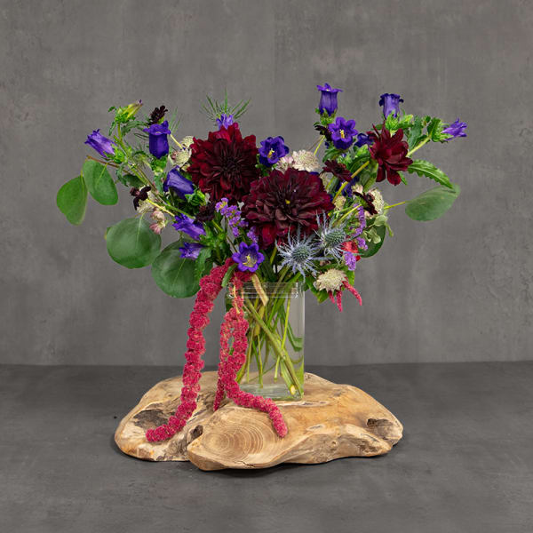 Purple and burgundy flowers in a clear glass vase on a wood slab