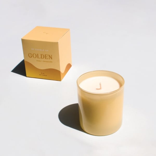 Gold candle in a glass jar beside its box