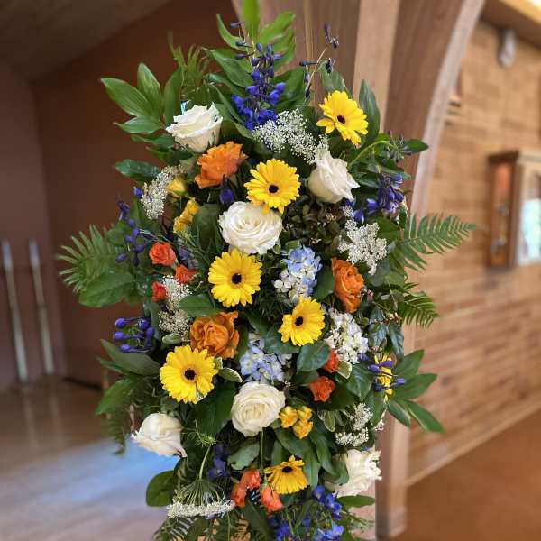 Standing floral spray with yellow daisies, white roses, and blue flowers