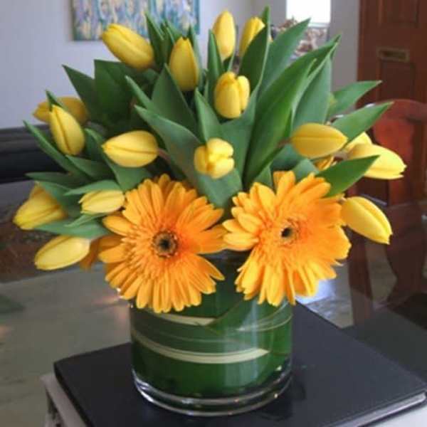 Yellow tulips and orange gerbera daisies in a glass vase