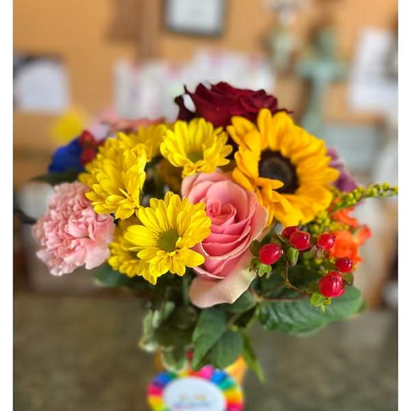 Mixed bouquet with sunflowers, roses, and pink carnations in a glass vase
