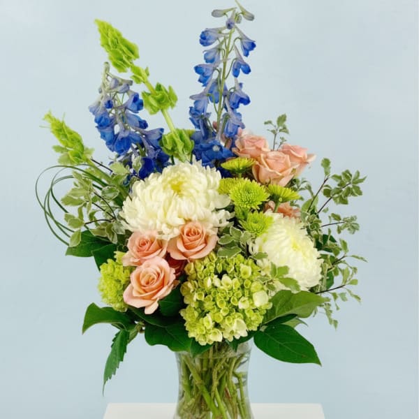 Mixed bouquet in a clear glass vase with blue, peach, and white blooms
