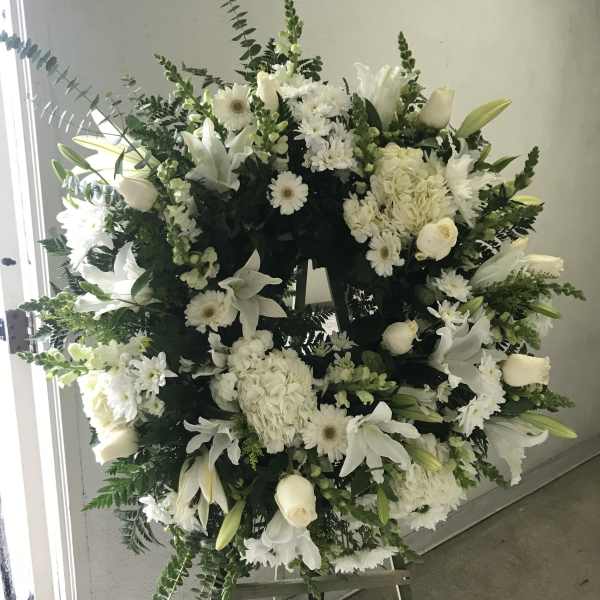 Large white funeral wreath on an easel with lilies and roses